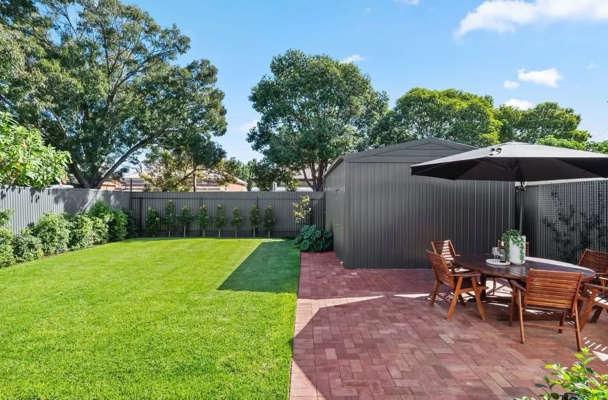 Yard Theory backyard with a green lawn, brick-paved patio, outdoor dining set and a charcoal shed