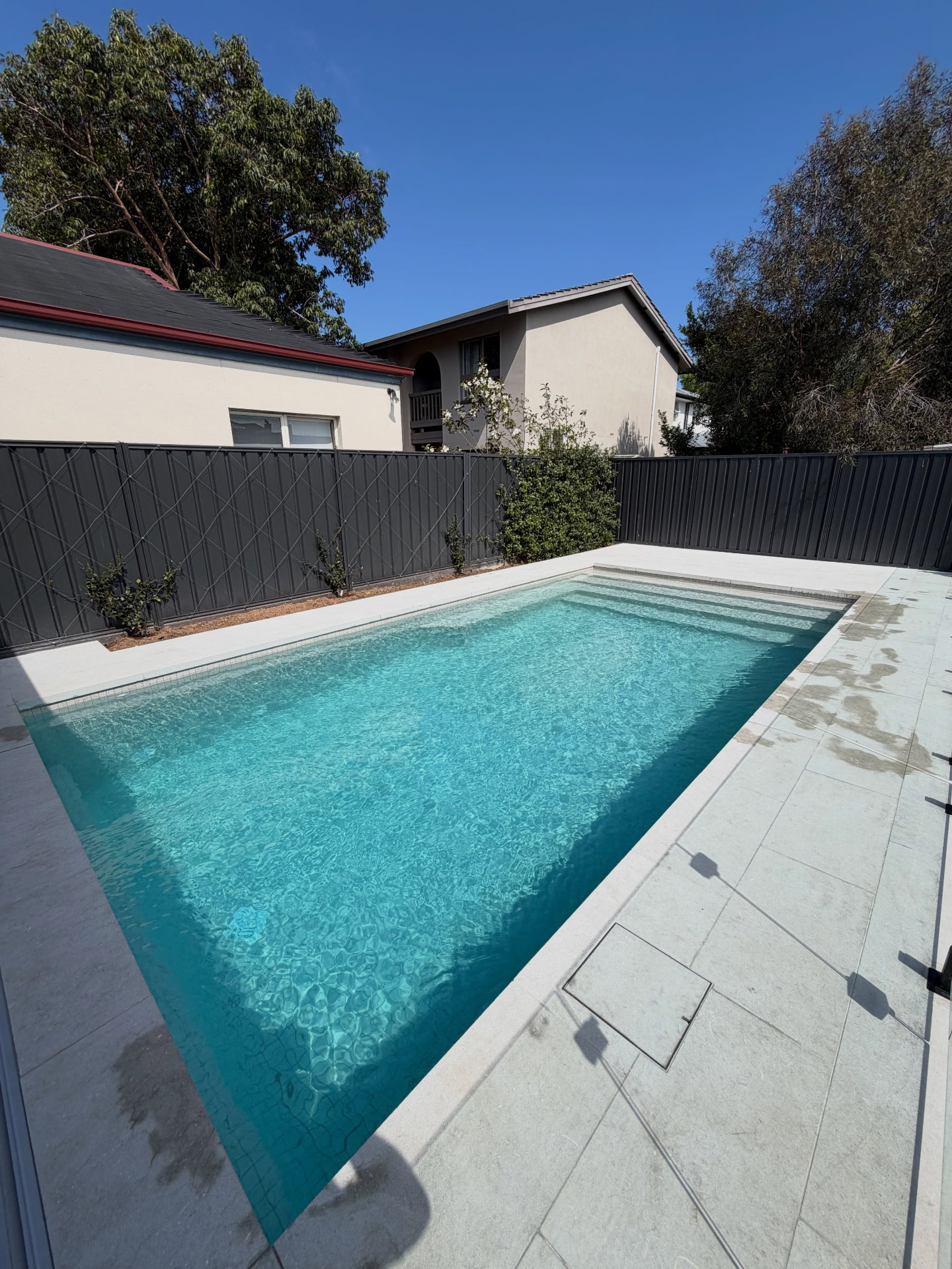 Poolside area with large light grey paving around a swimming pool and a band of mosaic tiles at the waterline
